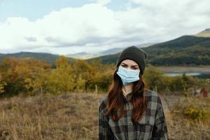 op reis in een warm hoed en een medisch masker in de bergen in een herfst weide foto