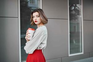 mooi vrouw in rood rok in de buurt gebouw heet drinken foto