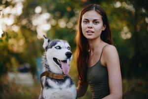 een vrouw met een schor ras hond glimlacht en liefdevol beroertes haar geliefde hond terwijl wandelen in natuur in de park in herfst tegen de backdrop van zonsondergang foto