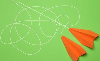twee papier oranje vliegtuigen met verschillend trajecten Aan een groen achtergrond, de het beste oplossing in bedrijf foto
