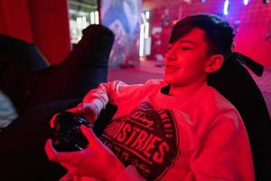 tiener jongen gamer Speel gamepad video spel troosten in rood gaming kamer. foto