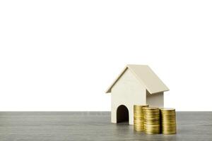 een klein houten huis model- met stack van gouden munten Aan hout tafel geïsoleerd Aan wit achtergrond. foto