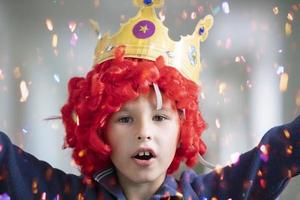 kind in een rood pruik en een kroon. clown jongen in glimmend snoep foto