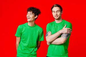 blij vrienden in groen t-shirts zijn staand De volgende naar rood achtergrond foto