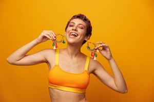 portret van een jong vrouw met een kort kapsel en gekleurde haar- glimlachen en tonen haar tong Bij de camera Aan een oranje achtergrond met oorbellen accessoires in de studio foto