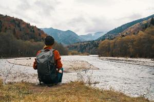 vrouw wandelaar zit Aan de rivier- bank en bewondert de berg landschap in de afstand terug visie foto