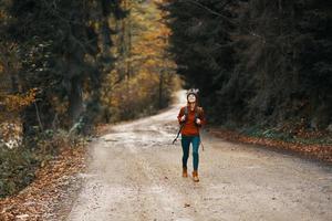 energiek vrouw rennen langs de weg met rugzak in herfst Woud foto