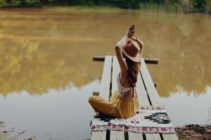 een vrouw yogi zit met haar terug naar de oever van de rivier Aan een brug en mediteert Aan ontspannende haar lichaam in natuur foto