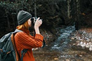 vrouw fotograaf Holding een camera in hand- in de buurt de rivier- in de bergen en Woud in de achtergrond foto