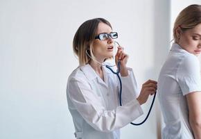 dokter in een medisch japon met een stethoscoop onderzoekt een geduldig Aan een licht achtergrond foto