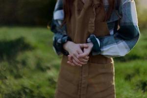 detailopname van een vrouw in een tuinman werk schort tegen de groente, vers zomer gras buitenshuis tonen haar handen foto