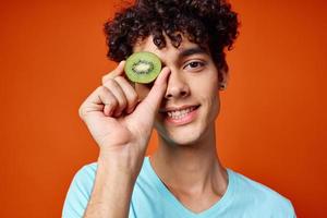 vrolijk vent met gekruld haar- kiwi in de buurt de ogen fruit detailopname foto