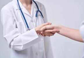 professioneel dokter vrouw schudt hand- van een vrouw geduldig Aan een licht achtergrond foto
