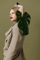 modieus vrouw in jas rood lippen mode palm blad groen achtergrond foto