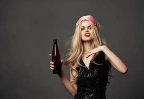 mooi blond met een fles van bier in haar hand- en een roze masker Aan haar hoofd foto