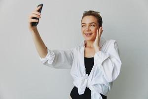 tiener- meisje blogger duurt foto's en schiet. haarzelf Aan video Aan haar telefoon voor sociaal media inhoud, video blogger, selfies tegen een wit muur met een glimlach Bij huis, freelancer foto