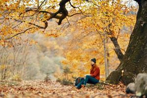 vrouw met rugzak in herfst Woud zittend in de buurt boom landschap vers lucht park foto