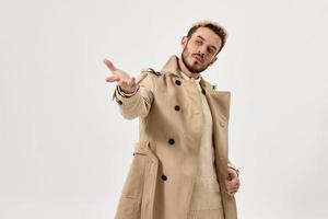 Mens in beige jas gebaren met hand- emoties studio mode licht achtergrond foto
