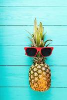 ananas met rood zonnebril Aan een blauw houten tafel. top visie en selectief focus foto