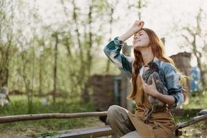 een vrouw onderzoekt een kip in haar handen en wrijft haar voorhoofd van de vermoeidheid van werken Aan een boerderij en zorgzaam voor de vogelstand ze feeds biologisch foto