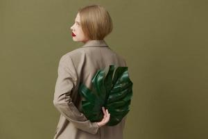 portret van een vrouw in jas rood lippen mode palm blad groen achtergrond foto