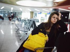 vrouw met verdrietig gelaats uitdrukking luchthaven aan het wachten geel rugzak foto
