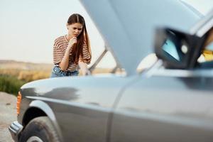 een vrouw reiziger staat door haar oud auto met de kap open, op zoek voor de oorzaak van de auto afbreken alleen zonder mannen Aan de weg in de platteland foto