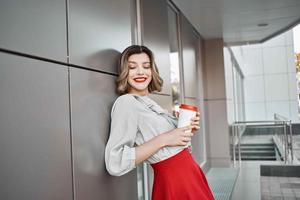 vrouw in rood rok kop van koffie poseren buitenshuis in de buurt gebouw foto