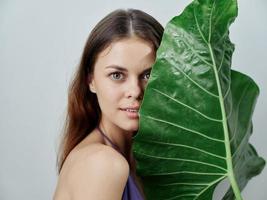 vrouw Holding een groen groot blad in de buurt haar gezicht aantrekkelijk kijken naakt schouders detailopname foto