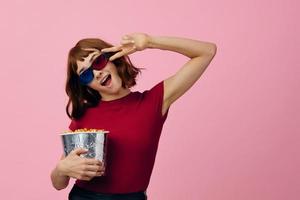 dolblij gelukkig schattig roodharige dame in rood t-shirt 3d bril met popcorn kijk maar film poseren geïsoleerd Aan over- roze studio achtergrond. kopiëren ruimte spandoek. mode bioscoop concept. vermaak aanbod foto