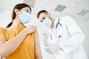 dokter maakt een injectie in de schouder van een geduldig in een medisch masker bodem visie covid vaccinatie foto