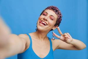 jong sport- vrouw mode blogger duurt een afbeelding van haarzelf Aan de telefoon in blauw sportkleding glimlachen en tonen haar tong Aan een blauw monochroom achtergrond foto