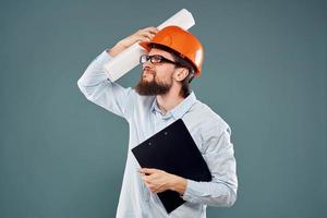 een mannetje ingenieur in een oranje moeilijk hoed met documenten in de handen van bouw tekeningen foto