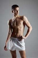 Mens bodybuilder in wit shorts gebaren met handen Aan grijs achtergrond sport geschiktheid model- foto