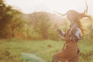 een vrouw rennen door een veld- Aan een zomer dag met lang vloeiende haar- in de stralen van de instelling zon. de concept van vrijheid en harmonie met natuur foto