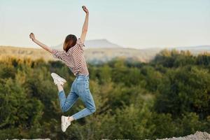 gelukkig vrouw jumping omhoog van geluk in natuur met haar terug naar de camera met een mooi berg visie foto