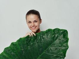 glimlachen vrouw Holding een groen blad in voorkant van haar licht achtergrond exotisch foto