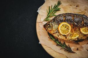 gebakken vis in oven met citroen en rozemarijn gelegd uit snijdend bord en perkament papier.op donker achtergrond. foto