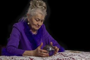 ouderen vrouw goochelaar met een glas bal. waarzegster Bij werk. foto