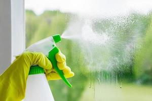 een vrouw spuit een schoonmaakmiddel op glas foto