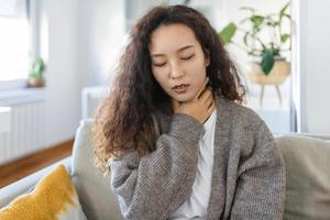 dichtbij omhoog van jong Aziatisch vrouw wrijven haar ontstoken amandelen, amandelontsteking probleem, bijgesneden. vrouw met schildklier klier probleem, aanraken haar nek, meisje heeft een zeer keel foto