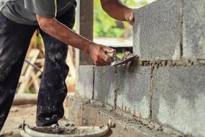hand- van arbeider bepleistering cement Aan steen muur Bij bouw plaats foto