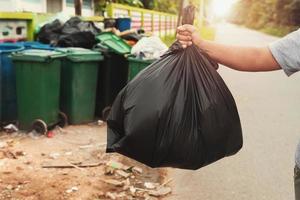 vrouw hand- Holding vuilnis in zwart zak voor schoonmaak in naar uitschot foto