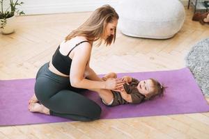 jong vrouw fit mam met baby meisje aan het doen opdrachten met massage bal Aan mat Bij huis foto