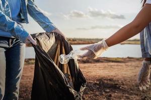 mensen vrijwilliger houden vuilnis plastic fles in zwart zak Bij park in de buurt rivier- in zonsondergang foto