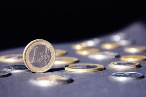 een euro munt staand Aan rand schijnend in spotlight tegen veel verschillend munten Aan donker achtergrond. geld stromen foto