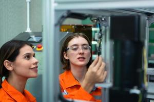 beide van vrouw in een elektronisch onderdelen fabriek gebruik makend van een productie lijn controleur en zijn aanbevelen collega's naar gebruik deze hulpmiddel. foto