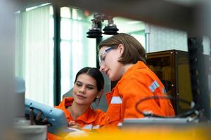 in een elektronisch onderdelen faciliteit, twee vrouw ingenieurs in de plant, inspecteren en testen robot handen gebruikt in de productie van elektronisch componenten. foto