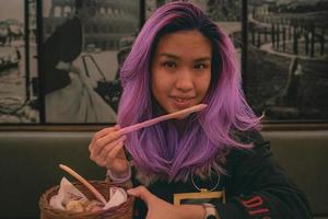 Purper haar- Aziatisch vrouw aan het eten een broodstengel Bij de Italiaans restaurant foto
