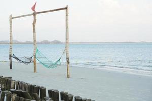 leeg schommel geweven door touw hangende Aan de houten polen Aan de strand met zeegezicht achtergrond foto